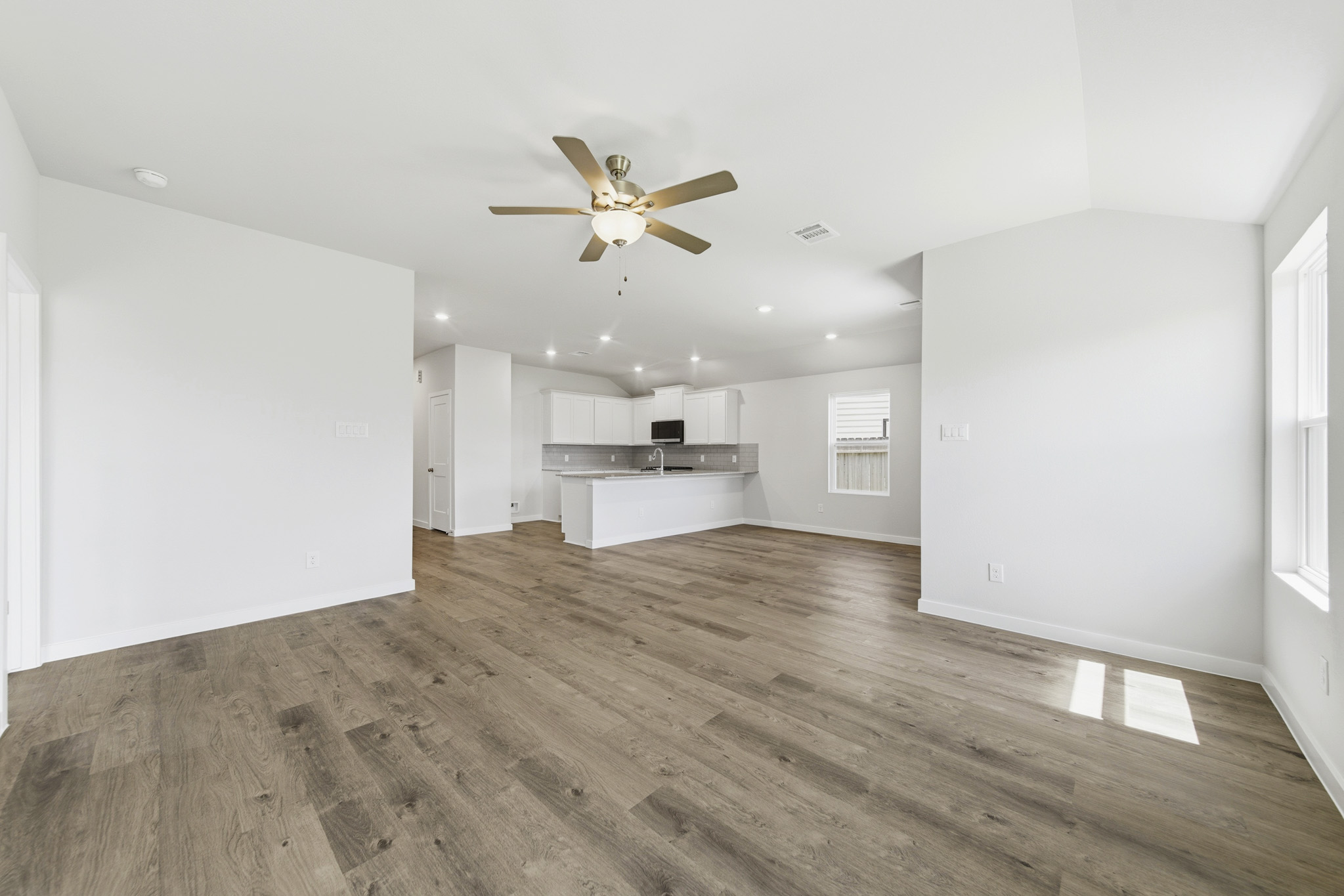 A large empty room with a wood floor and a ceiling fan.