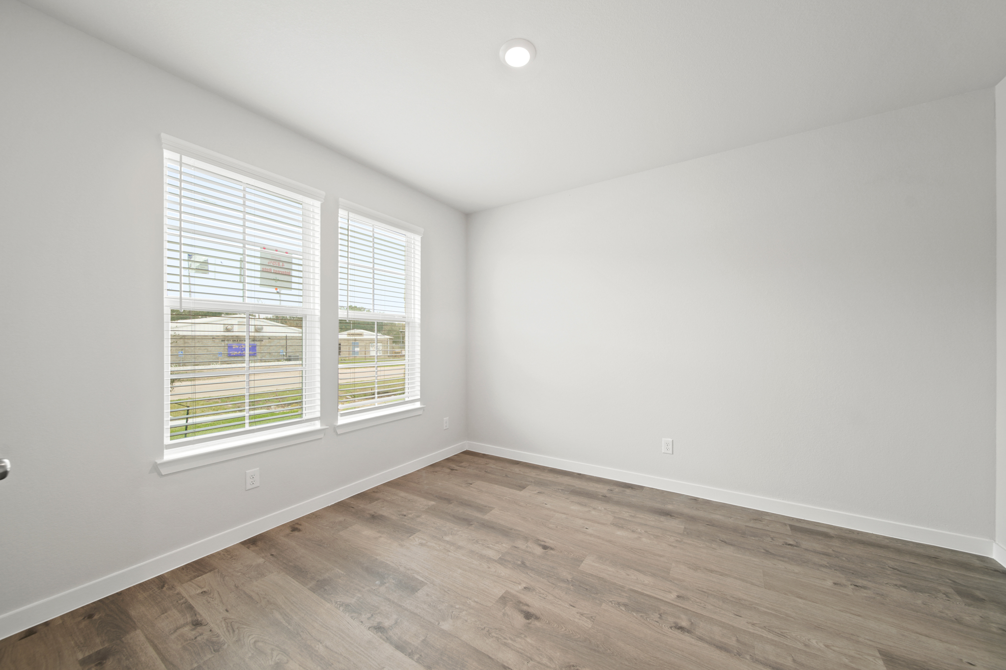 A room with a wood floor and a window with blinds.